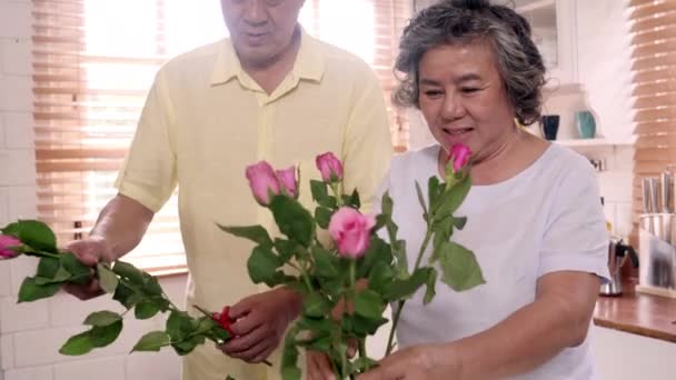アジアの高齢夫婦が自宅の台所の木製のテーブルに花束を作る 時間を使った中国の甘いシニアカップルは 自宅で一緒にリラックスします 家庭コンセプトのライフスタイルシニアカップル — ストック動画