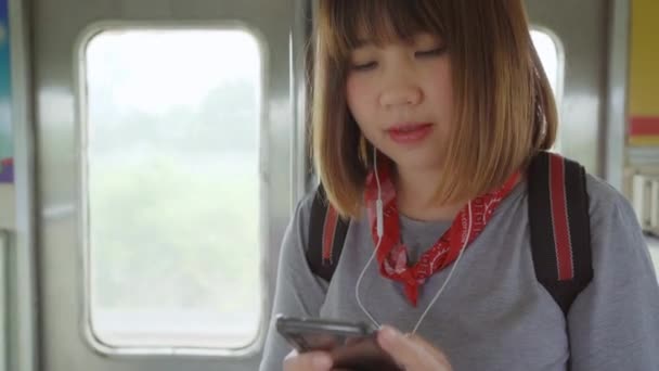 旅行アジアの女性を使用してスマート フォンの音楽を聴く列車ながら 若い女性観光客のバックパッカーがタイで彼女の旅をお楽しみください ライフ スタイル 代の女性はリラックスして旅行のコンセプト — ストック動画