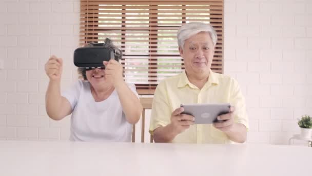 亚洲老年夫妇使用平板电脑和虚拟现实模拟器在客厅玩游戏 夫妇俩开心地利用时间一起躺在家里的桌子上 生活方式 家庭老年家庭概念 — 图库视频影像