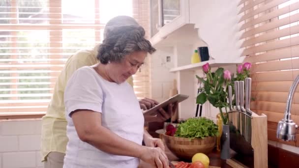 アジアの高齢夫婦カットトマトは 台所で食べ物を作るための成分を準備し カップルは自宅で健康的な食品のために有機野菜を使用しています 家庭で食べ物を作るライフスタイルシニアファミリー — ストック動画