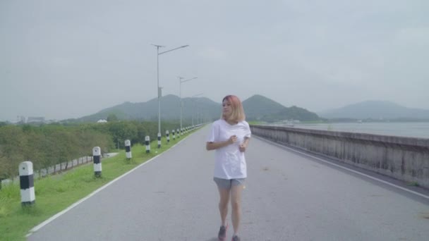 亚洲跑步女子在街头跑步和慢跑 健康美丽的年轻运动女性运动在湖边 生活方式适合和积极的妇女在街头的概念锻炼 — 图库视频影像