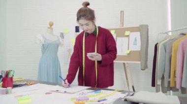Profesyonel güzel Asyalı kadın moda kumaş çizimler ile çalışma ve cep telefonuyla tasarımcı çizim giyim tasarım stüdyoda bul. Yaşam tarzı kadın kavramı çalışma.