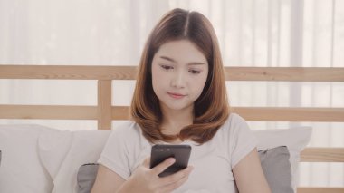 Genç Asyalı kadın uyan sabah, sonra yatakta yatıyordu süre Smartphone kullanarak gülümseyen güzel çekici Japon kız evde yatak odasında rahatlayın. Ev concept zaman yaşam tarzı kadınlar enjoying.