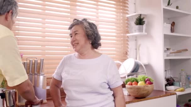 アジアの高齢夫婦が自宅の台所で朝食をとる 中国の甘いカップルの男性は 自宅で彼の妻にクッキーを供給しています 在宅ライフスタイルシニアファミリーコンセプト — ストック動画