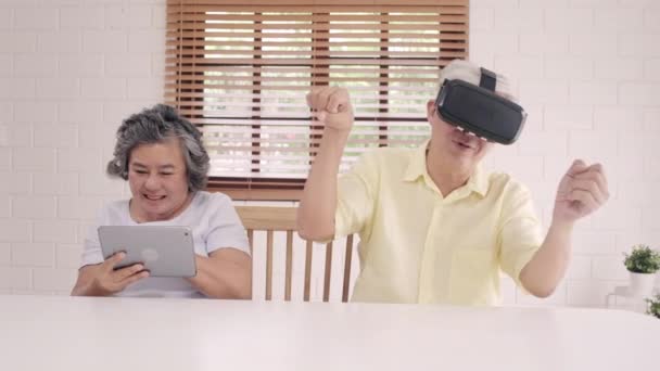 亚洲老年夫妇使用平板电脑和虚拟现实模拟器在客厅玩游戏 夫妇俩开心地利用时间一起躺在家里的桌子上 生活方式 家庭老年家庭概念 — 图库视频影像