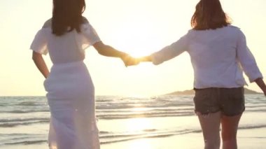 Genç Asyalı lezbiyen çift sahilde koşuyor. Güzel kadın arkadaşlar mutlu akşam gün batımında deniz kenarında plajda eğlenmek. Plaj konsepti lifestyle lezbiyen çift seyahat.