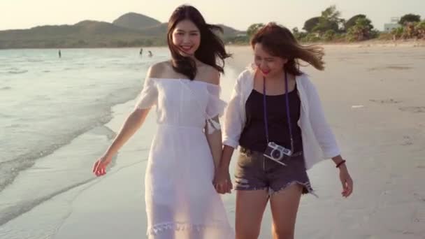ビーチを歩く若いアジアのレズビアンのカップル 美しい女性の友人は 夕方の夕日のときに海の近くのビーチでリラックスしてリラックスします ライフスタイル レズビアン カップルはビーチコンセプトで旅行 — ストック動画