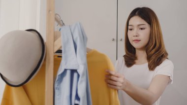 Evde dolap veya mağaza içinde onun moda kıyafet giysiler seçmek güzel çekici genç Asyalı kadın. Kız ne kazak giymeyi düşünüyorum. Ev dolap ya da soyunma giyim mağazası.