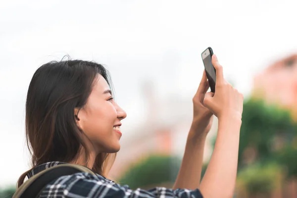 Matkailija reppumatkailija aasialainen nainen bloggaaja viettää lomamatkan hämmästyttävällä maamerkillä nauttia matkastaan perinteisessä kaupungissa ja käyttää älypuhelinta ottamaan kuvan matkustaessaan Bangkokissa, Thaimaassa . — kuvapankkivalokuva