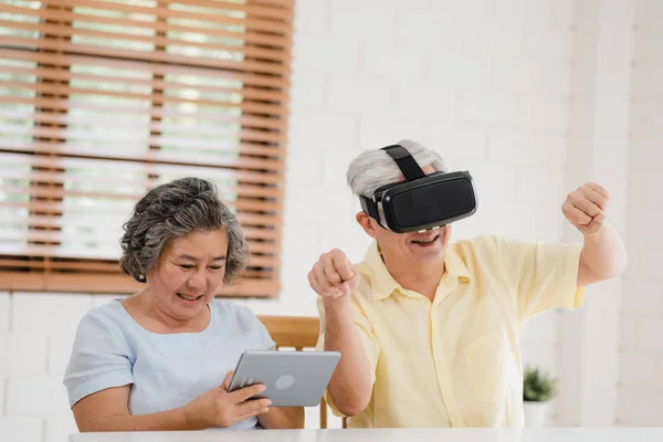 Asiatisches älteres Paar mit Tablet und Virtual-Reality-Simulator beim Spielen im Wohnzimmer, Paar, das sich glücklich fühlt, wenn es zu Hause auf dem Tisch liegt. Lifestyle Seniorenfamilie zu Hause Konzept. — Stockfoto