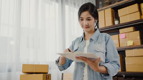 Frumos inteligent asiatic tânăr antreprenor femeie de afaceri proprietar de IMM-uri verificarea produsului pe stoc și scrie pe clipboard de lucru la domiciliu. Proprietar de afaceri mici la conceptul de birou de acasă . — Fotografie, imagine de stoc