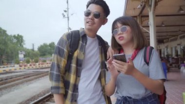 Tren istasyonunda Asya sırt çantası çift, Tayland kendi yolculuğunda cep telefonu görünümlü ve yön haritaları kullanarak Genç tatlı çift turist backpacker. Yaşam tarzları çift dinlenmek ve seyahat kavramı.