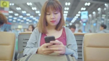 Yavaş hareket - kullanarak ve uçağının kalkış kapısı uluslararası havaalanında beklerken onun smartphone terminal salonunda kontrol mutlu Asyalı kadın. Kadınlar Havaalanı kavramında mutlu.