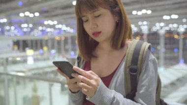 Kullanarak ve uçağının kalkış kapısı uluslararası havaalanında beklerken onun smartphone terminal salonunda kontrol mutlu Asyalı kadın. Kadınlar Havaalanı kavramında mutlu.