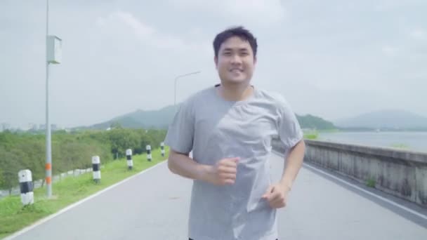 亚洲长跑男子在街上跑步和慢跑 健康英俊的年轻运动男性运动附近的湖 生活方式适合和活跃的男子锻炼街头概念 — 图库视频影像