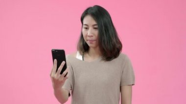 Genç Asyalı kadın pembe arka plan stüdyo çekim üzerinde rahat giyim gülümseyerek mutlu duygu sosyal medya kontrol akıllı telefon kullanarak. Mutlu gülümseyen sevimli mutlu kadın başarı sevinir.