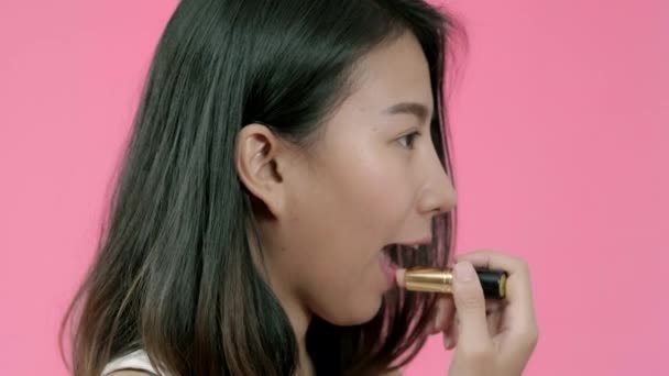 年轻美丽的时尚亚洲妇女应用嘴唇化妆与化妆刷在休闲服装粉红色背景工作室拍摄 快乐微笑可爱的快乐女人欢欣鼓舞成功 — 图库视频影像