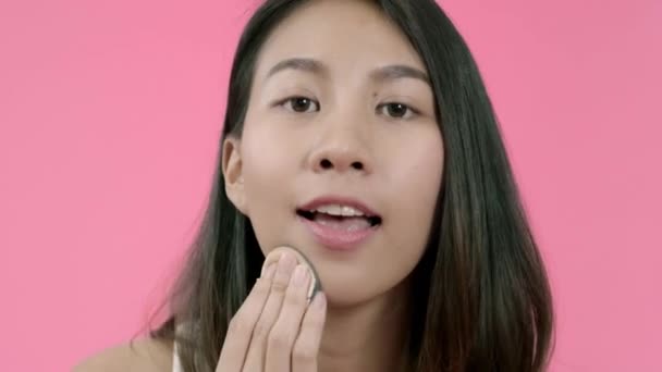 ピンクの背景スタジオショットの上にカジュアルな服で化粧品ブラシでパウダーメイクを適用若い美しいファッショナブルなアジアの女性 幸せな笑顔愛らしい喜んで女性は成功を喜ぶ — ストック動画