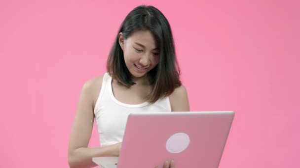 年轻的亚洲妇女工作在笔记本电脑检查社交媒体在休闲服装和看电脑在粉红色的背景工作室拍摄 快乐微笑可爱的快乐女人欢欣鼓舞成功 — 图库视频影像