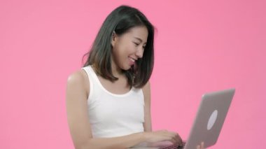 Dizüstü bilgisayar üzerinde çalışan genç Asyalı kadın rahat giyim sosyal medya kontrol ve pembe arka plan stüdyo çekim üzerinden kameraya bakarak. Mutlu heyecanlı sevimli mutlu kadın başarı sevinir.