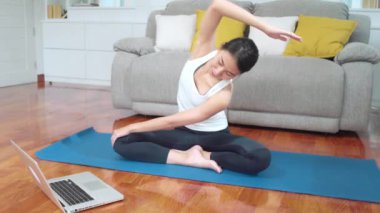 Asya yoga eğitmeni kadın evde oturma odasında yoga yapmak için nasıl canlı öğretim için dizüstü bilgisayar kullanarak. Fit vücut için genç sağlıklı kadın egzersiz. Evde kadın egzersiz kavramı.