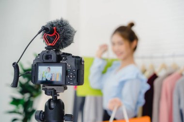 Asya moda kadın blogger online etki unsuru holding alışveriş torbaları ve giysi bir sürü yeni moda video yayını kaydetmek için giysi raf üzerinde canlı video evde sosyal ağ Internet tarafından için.