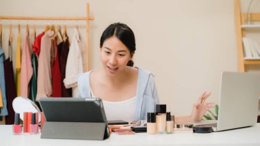 Güzellik blogger soru ve cevap-laptop önünde oturan video kayıt için tablet. Asyalı kadın kullanım kozmetik inceleme yapmak öğretici mutlu güzel genç sosyal ağ için canlı video yayını