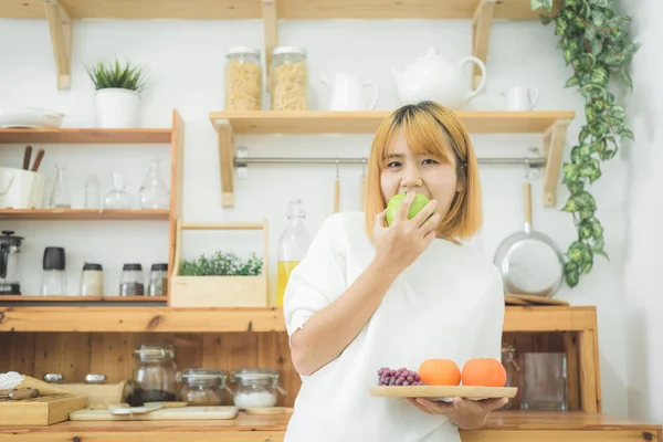 Asiatisk vakker kvinne med frukt og grønnsaker i kjøkkenet. Lykkelig, søt asiatisk kvinne spiser frisk frukt for en sunn kropp. livsstil asiatisk kvinne som hjemmebegrep . – stockfoto