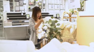 Genç Asyalı kadın depoda yeni mobilya seçerek alışveriş sepeti sürmek, genç kadın mağazada raflar önünde mutlu hissediyorum. Kadınlar alışveriş yeni mobilya konsepti.