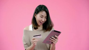 Kredi kartı ile online alışveriş satın tablet kullanan genç Asyalı kadın pembe arka plan stüdyo çekim üzerinde rahat giyim gülümseyerek mutlu hissediyorum. Mutlu gülümseyen sevimli mutlu kadın başarı sevinir.