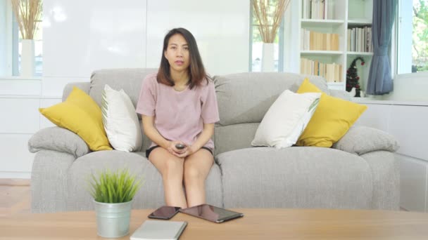 年轻的亚洲少女在家里看电视 女人躺在客厅的沙发上感到快乐 生活方式的女人早上在家休息一下 — 图库视频影像