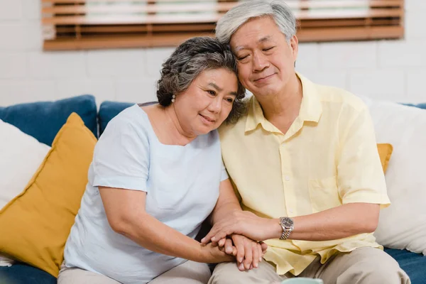 Ein älteres asiatisches Paar hält sich im Wohnzimmer an den Händen, ein Paar, das sich glücklich teilt und sich gegenseitig unterstützt, wenn es zu Hause auf dem Sofa liegt. Lifestyle Seniorenfamilie zu Hause Konzept. — Stockfoto