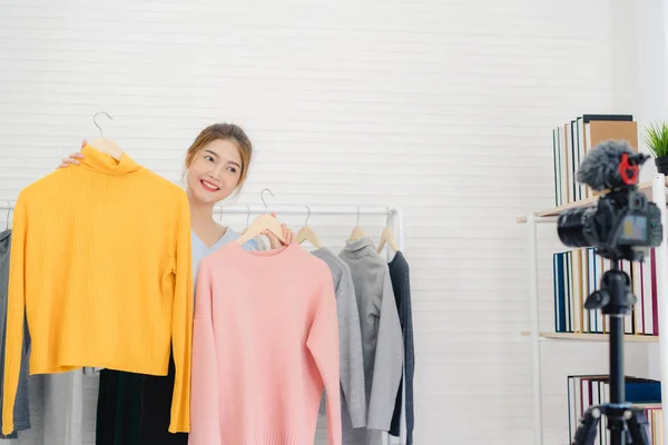 Blogueuse de mode asiatique influenceuse en ligne tenant des achats aBlogueuse de mode asiatique influenceuse en ligne tenant des sacs à provisions et beaucoup de vêtements sur le porte-vêtements pour enregistrer une nouvelle vidéo de mode diffusée en direct sur le réseau social par un stagiaire — Photo