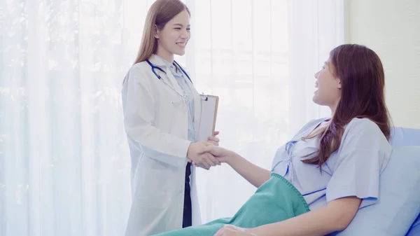 Vakker, smart asiatisk lege og pasient som diskuterer og forklarer noe med skriveplate i legens hender mens hun ligger på pasientens seng på sykehuset. Legemiddel- og helsebegrepet . – stockfoto