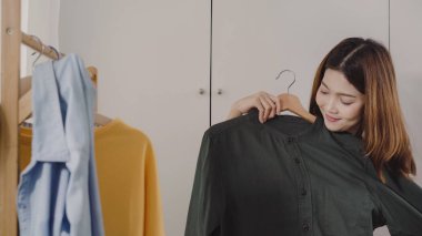 Evde dolap veya mağaza içinde onun moda kıyafet giysiler seçmek güzel çekici genç Asyalı kadın. Kız ne kazak giymeyi düşünüyorum. Ev dolap ya da soyunma giyim mağazası.