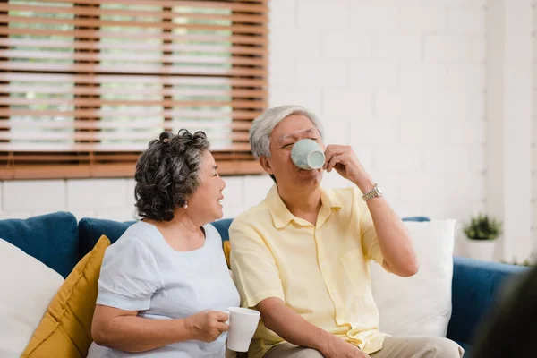 Asiatiska äldre par dricker varmt kaffe och pratar tillsammans i vardagsrummet hemma, par njuta av kärlek stund liggande på soffan när avslappnad hemma. Livsstil Senior familj at Home Concept. — Stockfoto