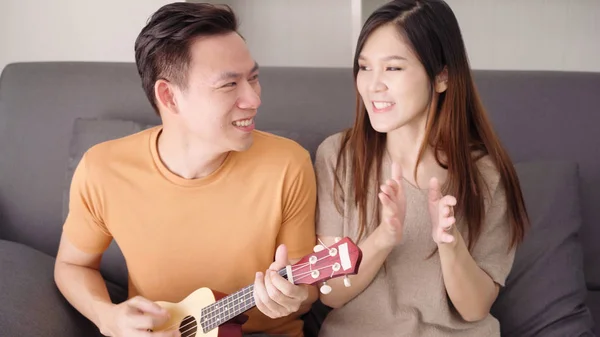 Couple asiatique jouant de la guitare et chantant ensemble dans le salon à la maison, couple doux profiter moment d'amour tout en étant couché sur le canapé quand se détendre à la maison. Mode de vie couple se détendre à la maison concept . — Photo