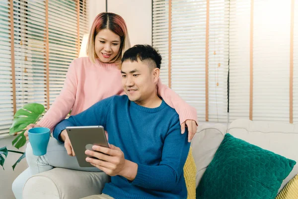 Atractiva pareja asiática dulce usando tableta mientras está acostado en el sofá cuando relajarse en su sala de estar en casa. Esposo y su esposa usando relajarse y tiempo romántico en el concepto de casa . — Foto de Stock
