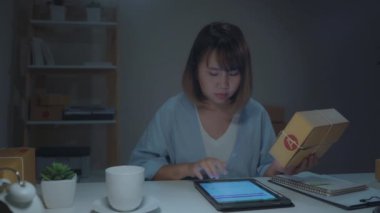 Stokta ürün kontrol Sme online Asyalı genç girişimci iş kadını sahibi ve tablet kaydetmek ve evde gece geç saatlerde çalışan kahve içme. Ev ofis konseptinde küçük işletme sahibi.