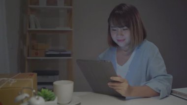 Stokta ürün kontrol Sme online Asyalı genç girişimci iş kadını sahibi ve tablet kaydetmek ve evde gece geç saatlerde çalışan kahve içme. Ev ofis konseptinde küçük işletme sahibi.