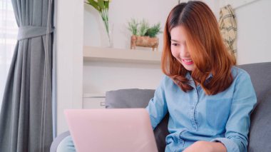 Kanepede yatan süre bilgisayar veya dizüstü bilgisayar kullanarak güzel çekici genç gülümseyen Asyalı kadın portresi ne zaman evde oturma odasında gevşeyin. Ev concept zaman yaşam tarzı kadınlar enjoying.