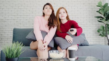 Lezbiyen Asyalı çift, TV gülmek izliyor ve evde oturma odasında patlamış mısır yemek tatlı çift evde rahat zaman kanepede yatarken komik anın tadını çıkarın. Yaşam tarzı çift evde kavramı relax.