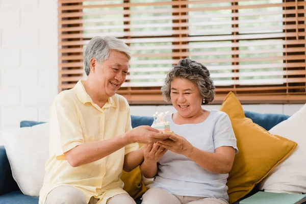 Ein älteres asiatisches Ehepaar mit Kuchen, der im heimischen Wohnzimmer den Geburtstag seiner Frau feiert. Japanisches Paar genießt Liebesmomente zusammen zu Hause. Lifestyle Seniorenfamilie zu Hause Konzept. — Stockfoto
