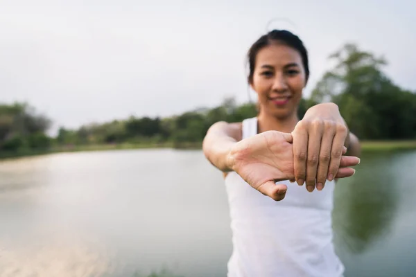 Saludable joven corredor asiático mujer caliente el cuerpo estiramiento antes del ejercicio y el yoga cerca del lago en el parque bajo la cálida luz de la mañana. Estilo de vida fitness y ejercicio activo de las mujeres en el concepto de ciudad urbana . — Foto de Stock