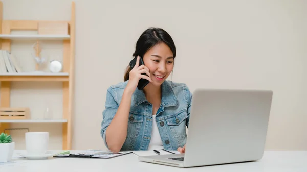 Hermosa mujer asiática de negocios inteligentes en ropa casual inteligente trabajando en el ordenador portátil y hablando por teléfono mientras está sentado en la mesa en la oficina creativa. Estilo de vida de las mujeres que trabajan en casa concepto . — Foto de Stock