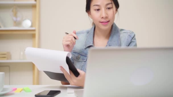美丽的年轻微笑的亚洲妇女工作笔记本电脑在客厅在家里 亚洲女商人在本家办公室写笔记本文件财务和计算器 享受在家的时间概念 — 图库视频影像