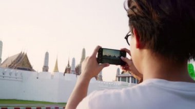 Bangkok tatil gezisi geçirirken bir fotoğraf çekmek için cep telefonu kullanarak Gezgin Asyalı adam, Tayland, erkek gün batımında inanılmaz dönüm noktasında yolculuk keyfini çıkarın. Yaşam tarzı erkekler şehir kavramı seyahat.