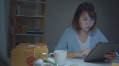 Stokta ürün kontrol Sme online Asyalı genç girişimci iş kadını sahibi ve tablet kaydetmek ve evde gece geç saatlerde çalışan kahve içme. Ev ofis konseptinde küçük işletme sahibi.