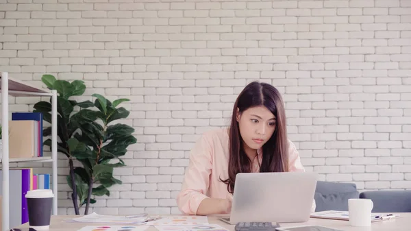 Vakker, ung, smilende asiatisk kvinne som jobber på pc-en i stua hjemme. En asiatisk forretningskvinne som skriver notatbok, finans og kalkulator på hjemmekontoret. Nyter tid hjemme-konseptet . – stockfoto