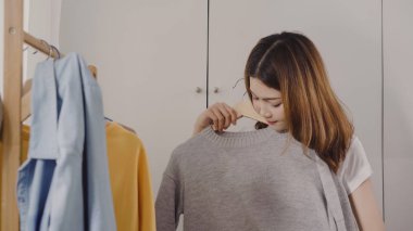 Evde dolap veya mağaza içinde onun moda kıyafet giysiler seçmek güzel çekici genç Asyalı kadın. Kız ne kazak giymeyi düşünüyorum. Ev dolap ya da soyunma giyim mağazası.